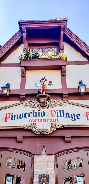 A charming Pinocchio Village restaurant entrance with Tudor-style architecture, lanterns, and window boxes filled with flowers.