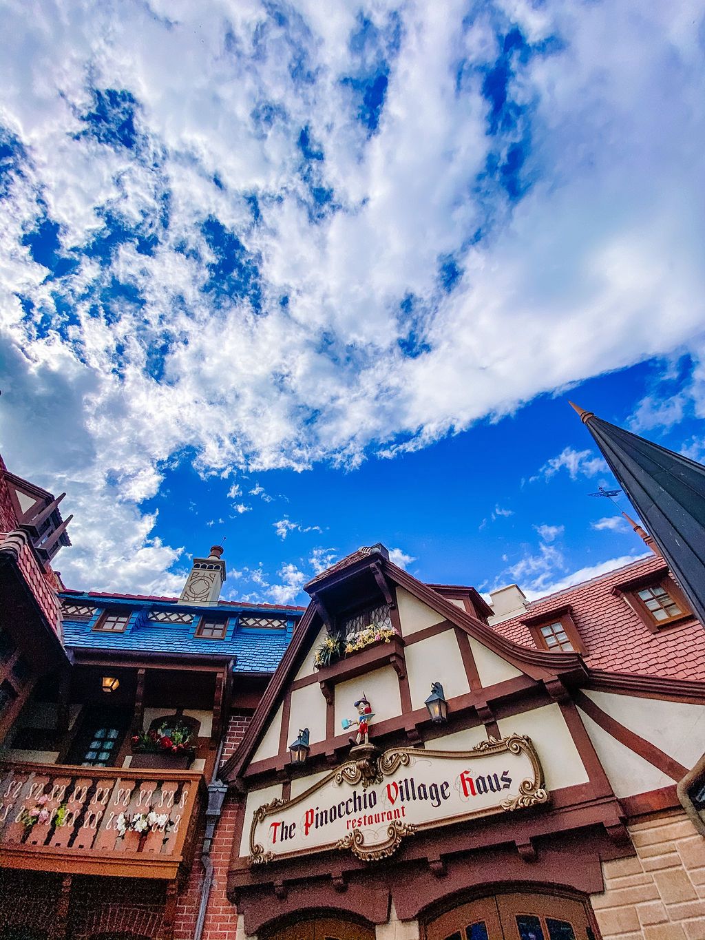 The Pinocchio Village Haus restaurant building with German-inspired architecture under dramatic blue skies and white clouds.
