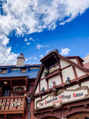 Bavarian-style German restaurant exterior with ornate wooden trim and signage under bright blue sky with white clouds.