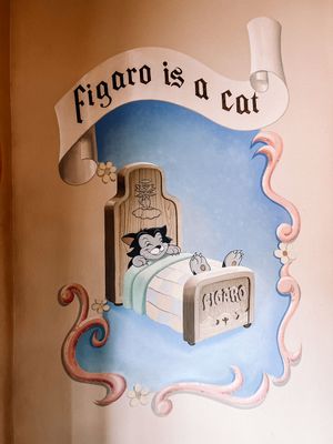 A whimsical mural painting on a wall shows a cat with curly decorative elements in a storybook style with blue sky accents.