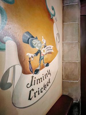 Vintage Jiminy Cricket art painted on a wall featuring the Disney character in a top hat reading from a book.