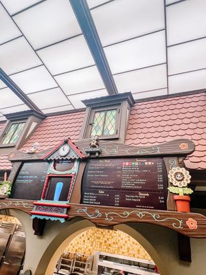 Pink-roofed decorative menu board with ornate woodwork and illuminated display panels at a theme park or fairground attraction.