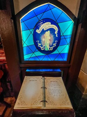 A vintage-style stained glass window with blue geometric patterns displaying a mystical emblem above an ornate open book.