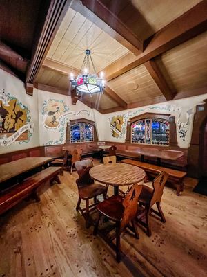 A cozy rustic attic dining room with wooden beams, round tables, and stained glass windows creates an intimate atmosphere.