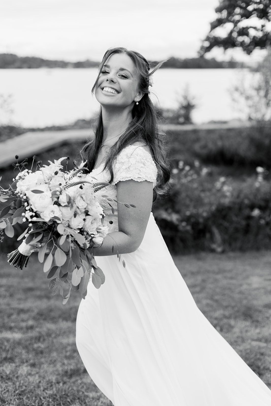 A joyful bride in a white wedding dress holds a lush bouquet of flowers while posing outdoors in black and white.