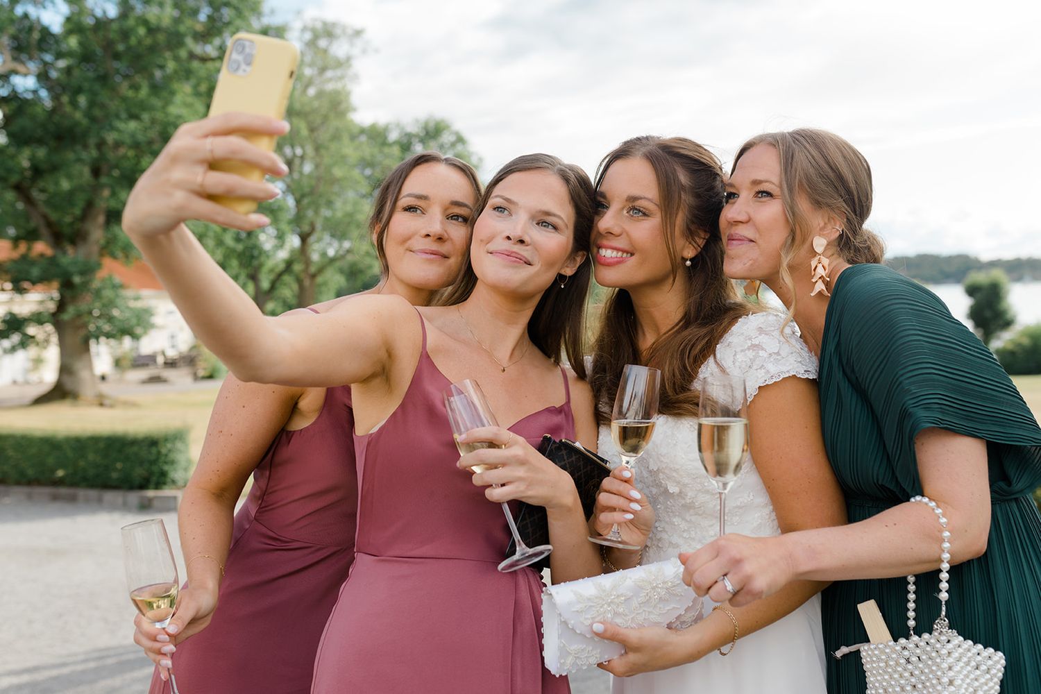 A group of friends in formal attire taking a selfie while holding champagne glasses at an outdoor event.