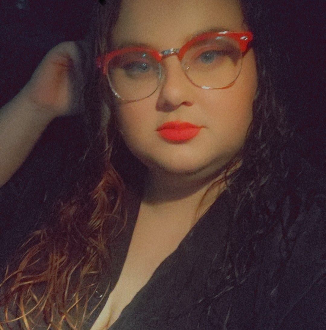 A selfie showing red cat-eye glasses frames and bright red lipstick in warm lighting.