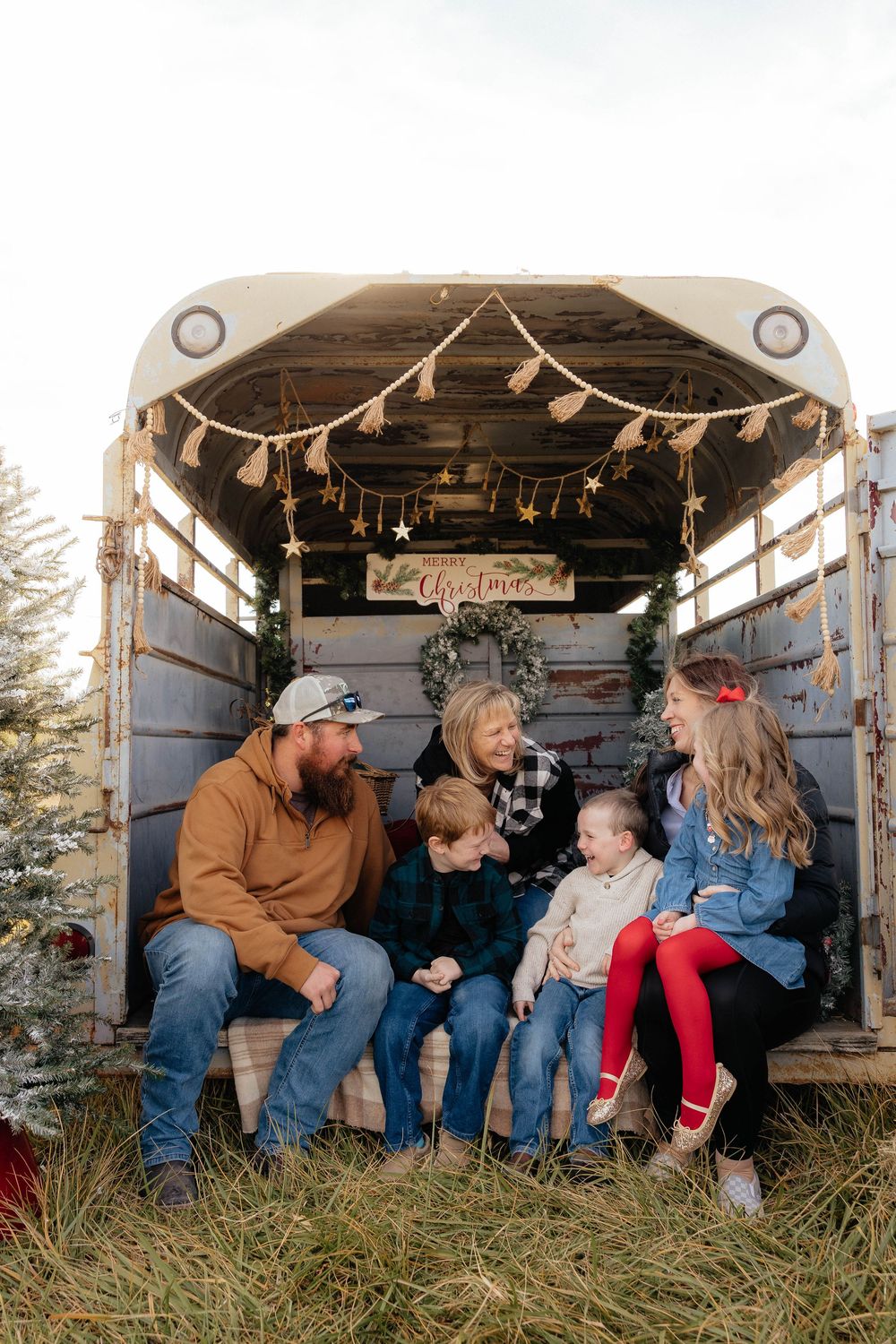 A family shares candid moments together while sitting in a rustic wooden trailer decorated for the holidays.