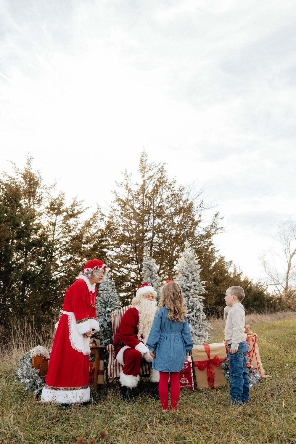 A group follows Santa Claus through a snowy field with evergreen trees in the background.