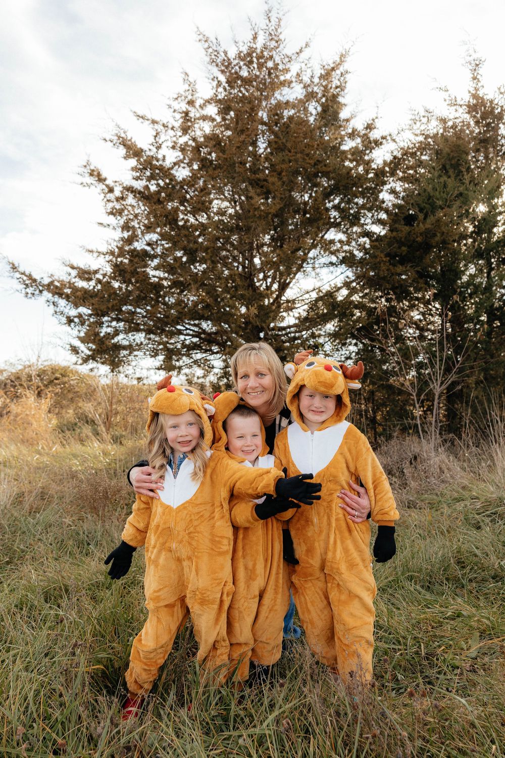 A group wearing matching yellow lion costumes poses together in a grassy field with autumn trees in the background.