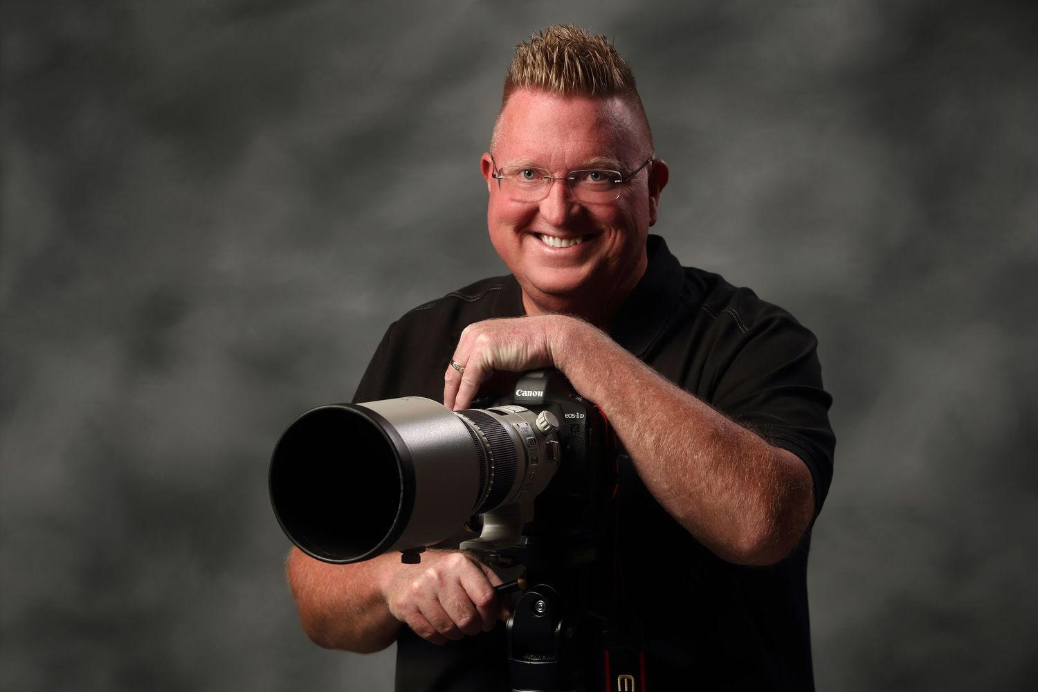 Professional photographer wearing black smiles while holding camera equipment in studio portraits.