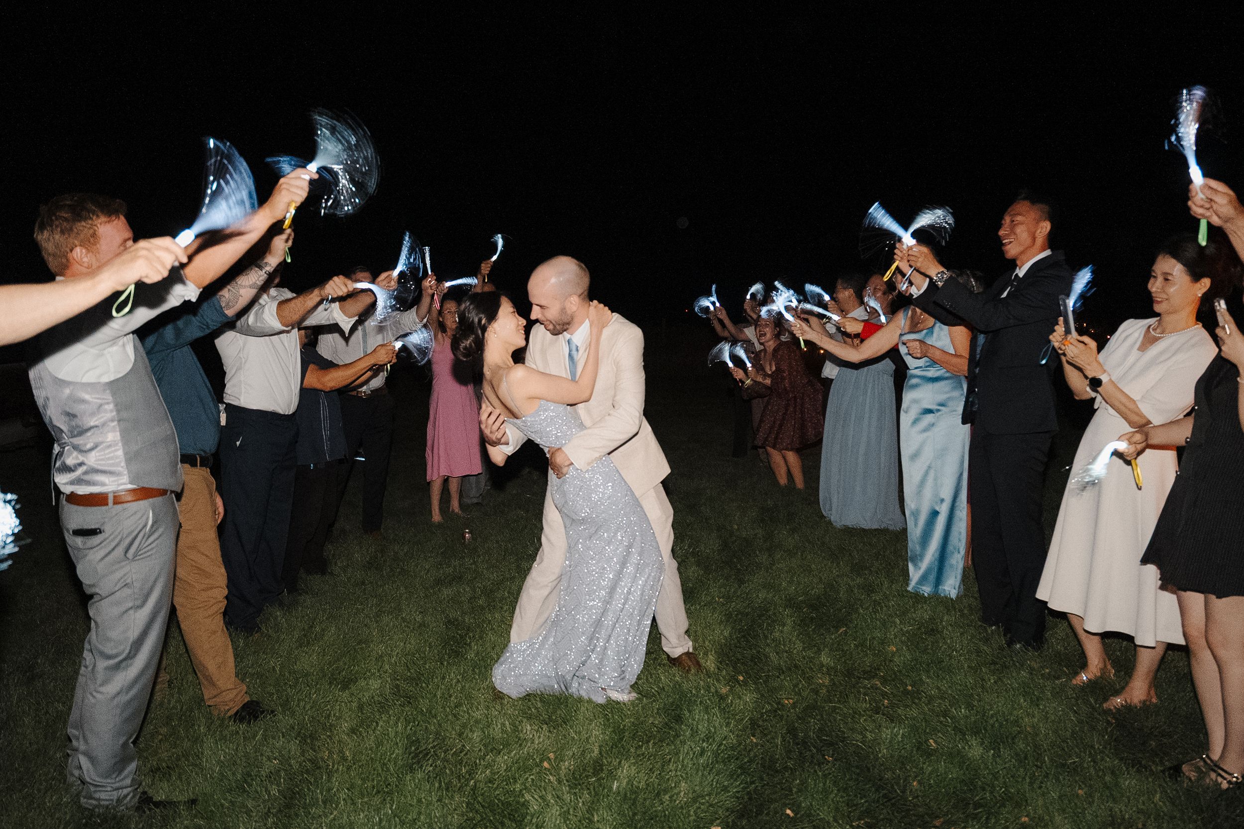 Wedding guests dancing and celebrating at night with sparklers on a lawn.