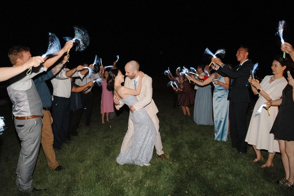 Wedding guests dancing and celebrating at night with sparklers on a lawn.