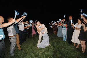 Wedding guests dance in a line formation on a grassy lawn at an outdoor evening reception.