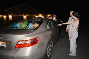 Person in protective suit and mask inspects a silver car at night with flashlight.