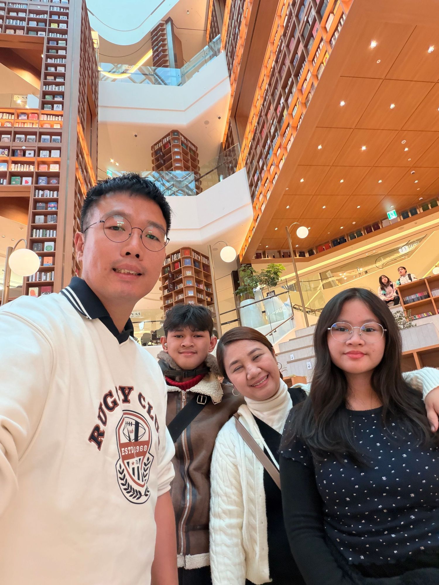 A group of friends pose together for selfies inside a shopping mall with brick walls and bright lighting.