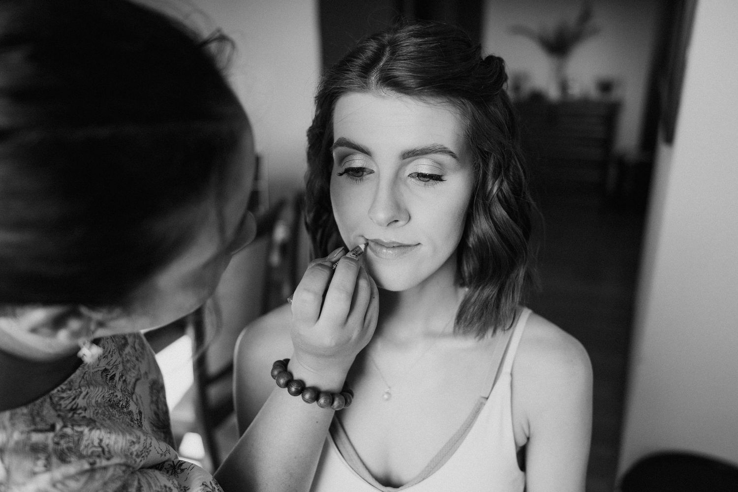 A black and white photo showing makeup being applied during wedding preparation.