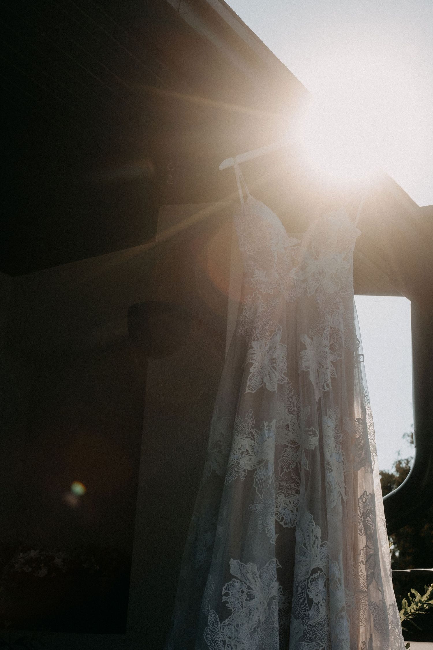 A white lace wedding dress hanging in dramatic sunlight.