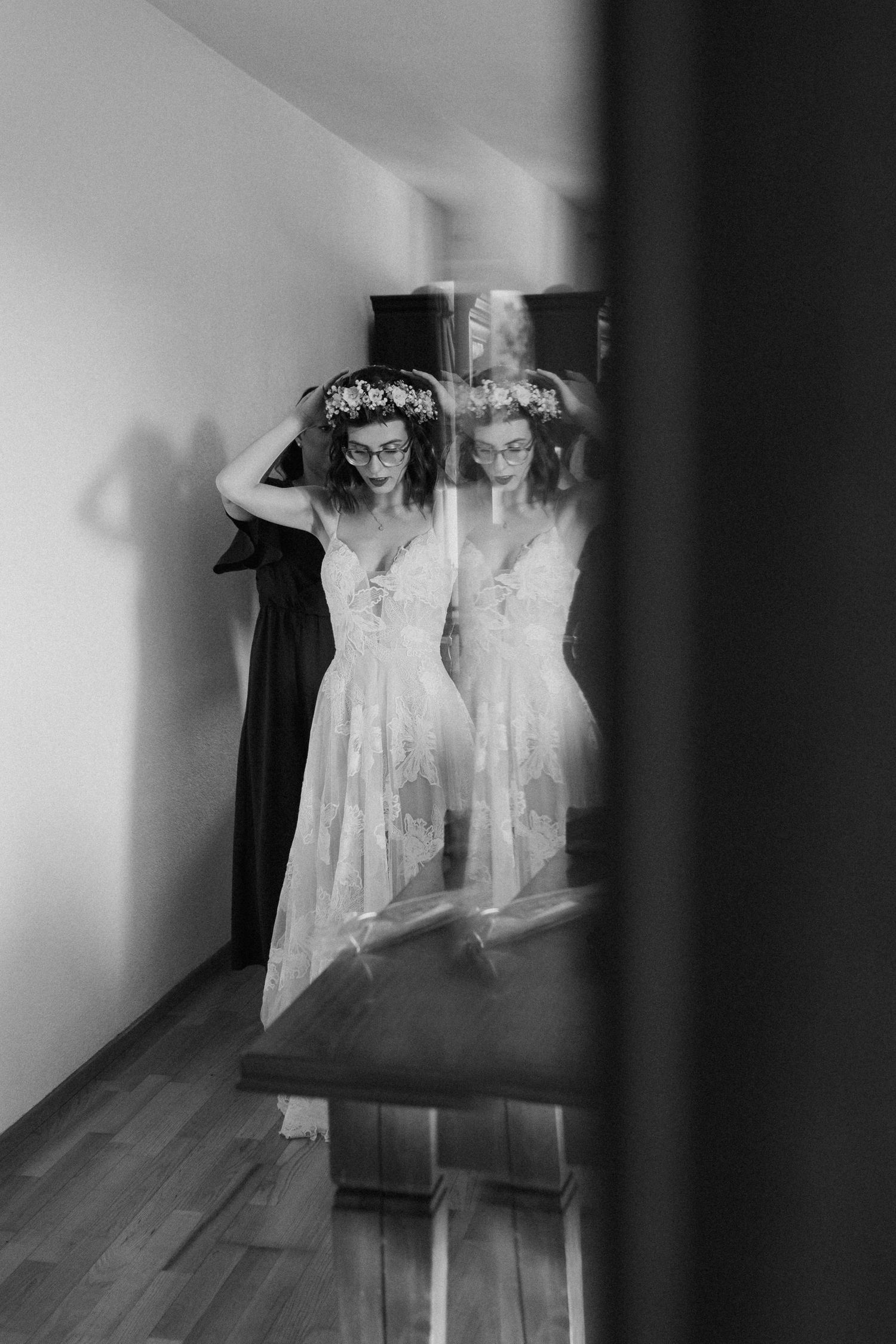 Black and white reflection of a bride in a lace dress looking in a mirror.