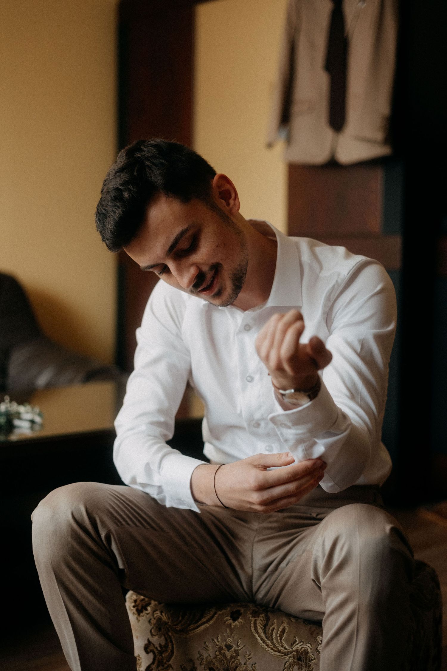 Person in white shirt buttoning cuffs while seated on ornate chair.