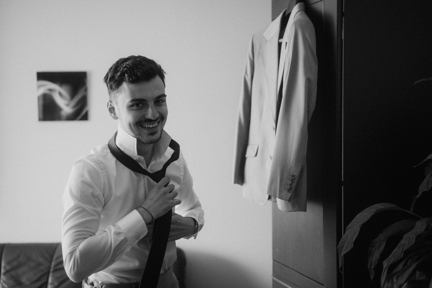 Person adjusting tie while getting dressed in formal attire.