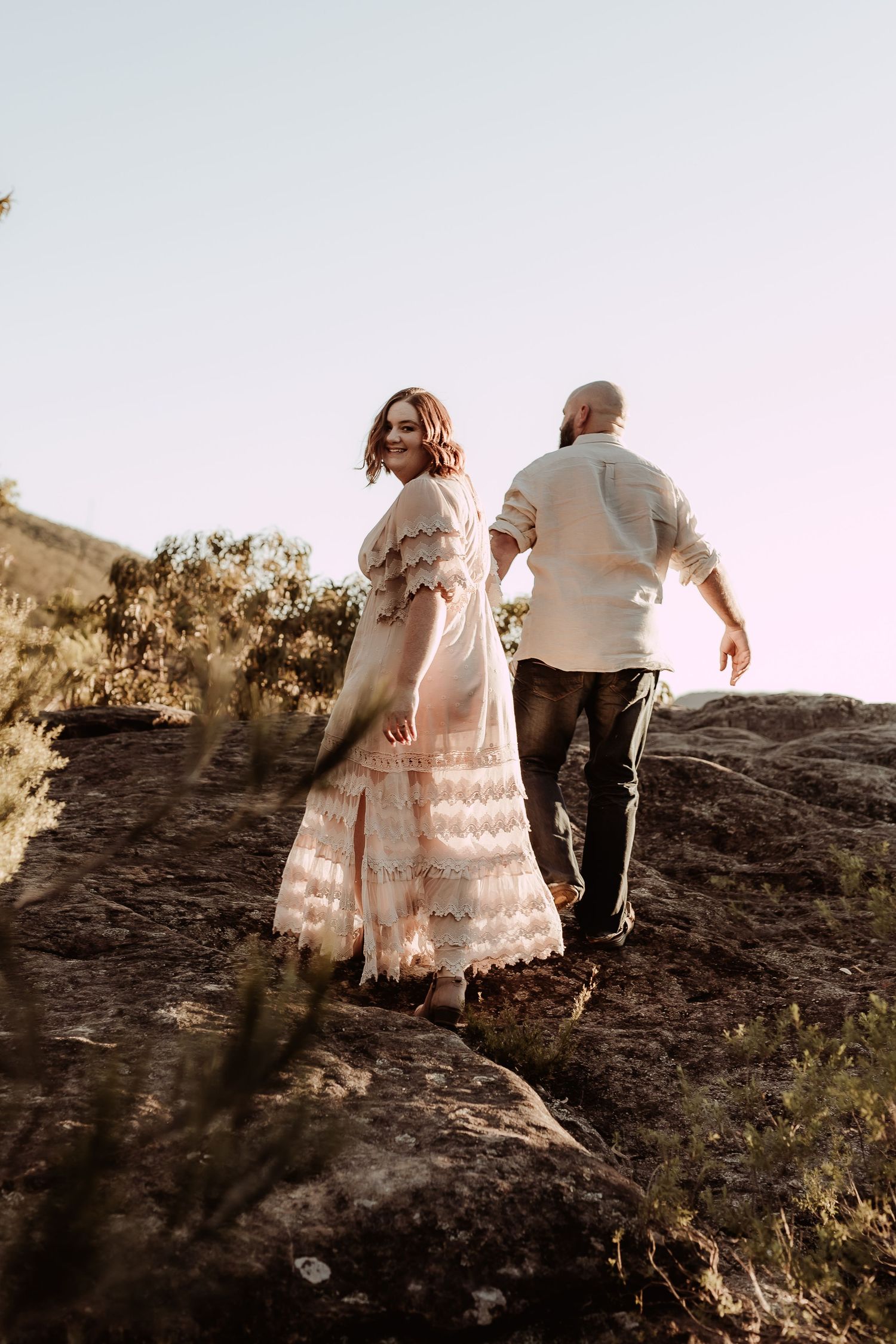 Couple walking together on rocky terrain during sunset.