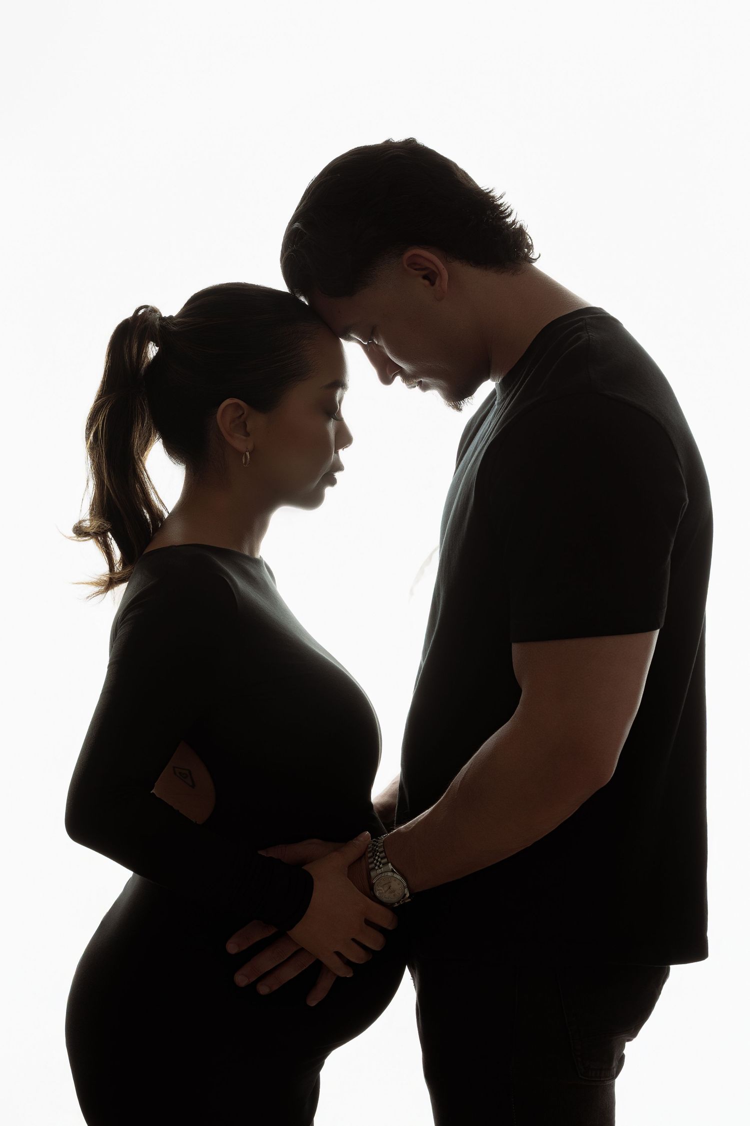 A series of sweet maternity photos showing a couple in matching white tops and light blue pants sharing tender moments together. Paloma