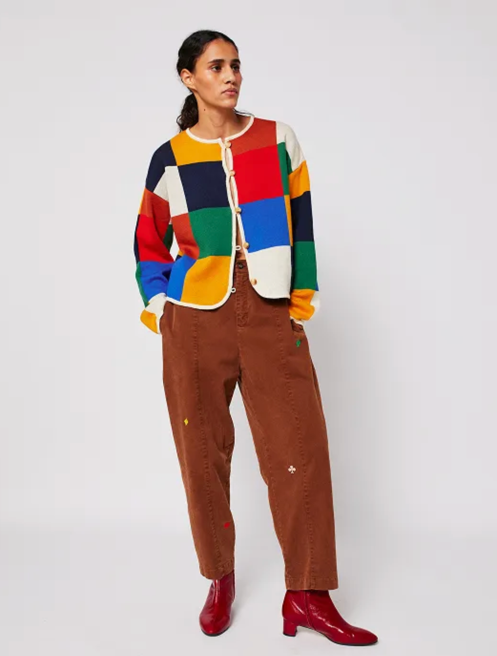 A colorful color-block cardigan styled with brown corduroy pants and red boots against a white background.
