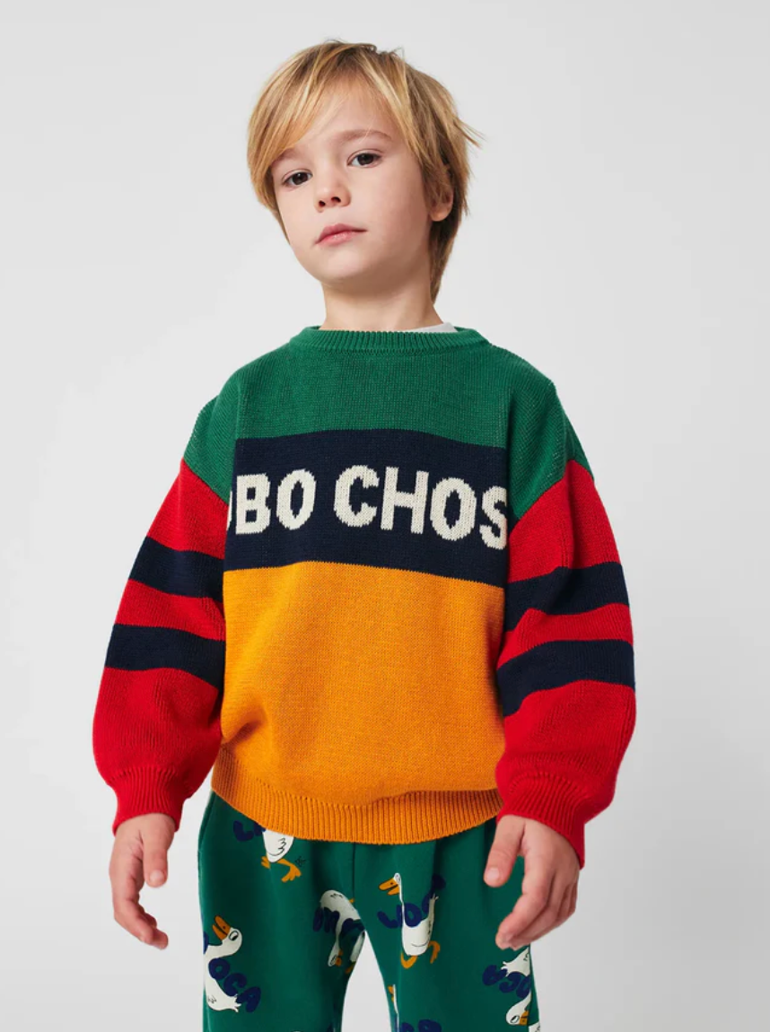 Colorful children's sweater with green, orange, and red color blocks paired with patterned pants.