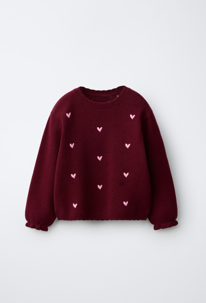 Burgundy knit girls sweater with scalloped edges, ruffled cuffs and small pink embroidered hearts scattered across the front.