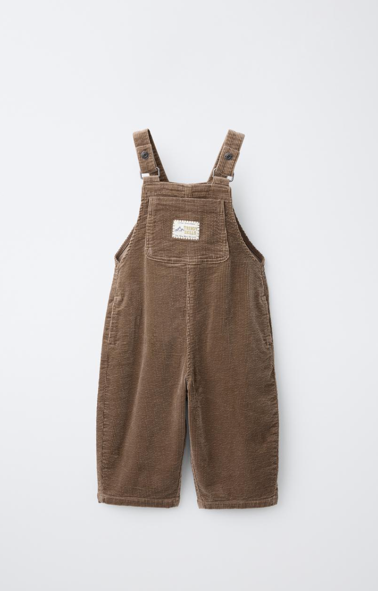 Brown corduroy baby overalls with adjustable shoulder straps, a front bib pocket with a small label, and a relaxed straight-leg fit.