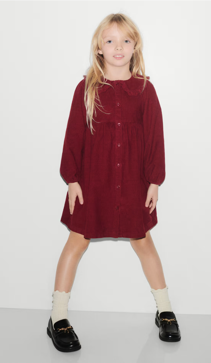 Girl wearing a burgundy button-front dress with ruffled collar and puff sleeves, styled with cream ruffle socks and black loafers.