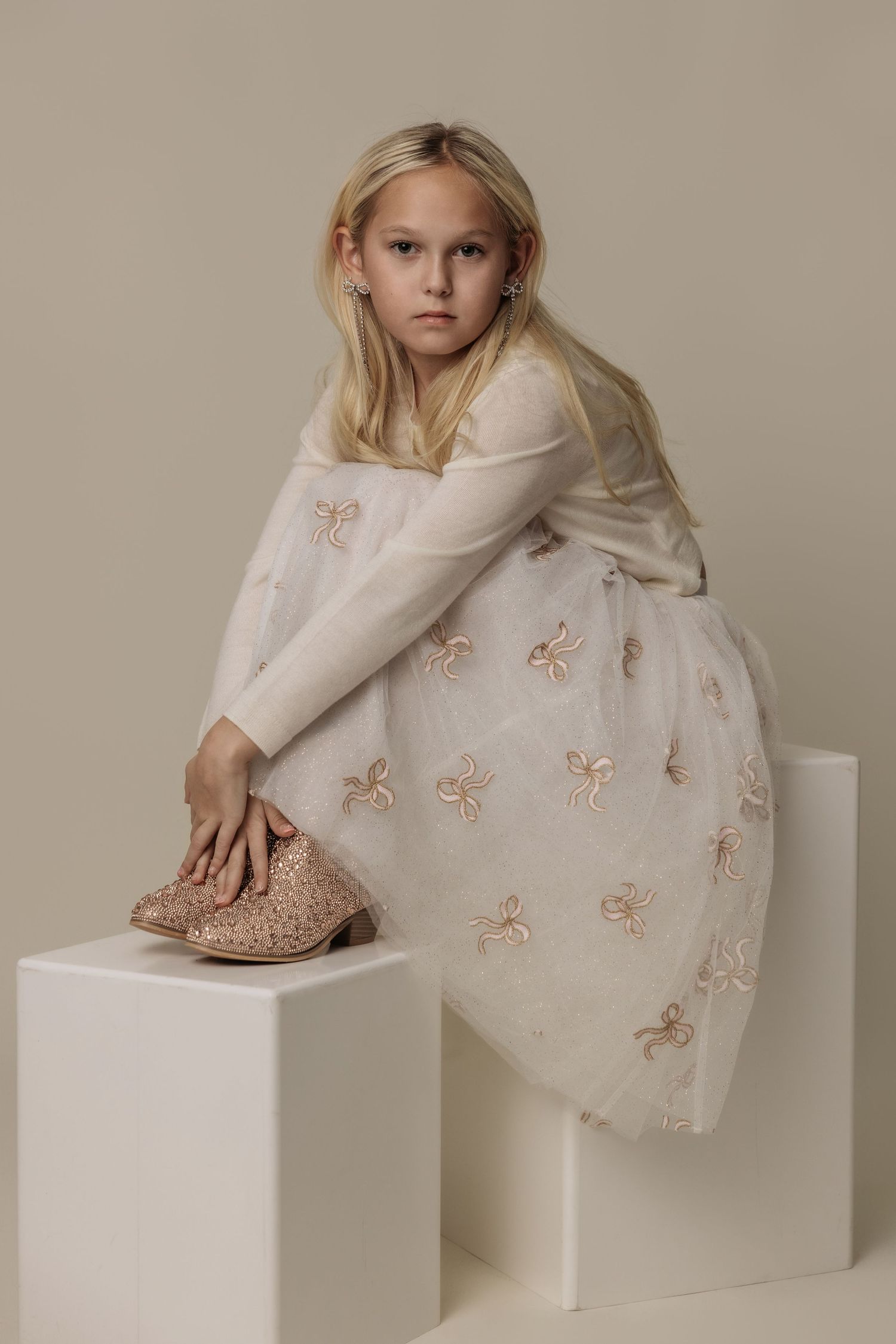 Artistic portrait series of a child posing on white blocks wearing a delicate embellished dress.