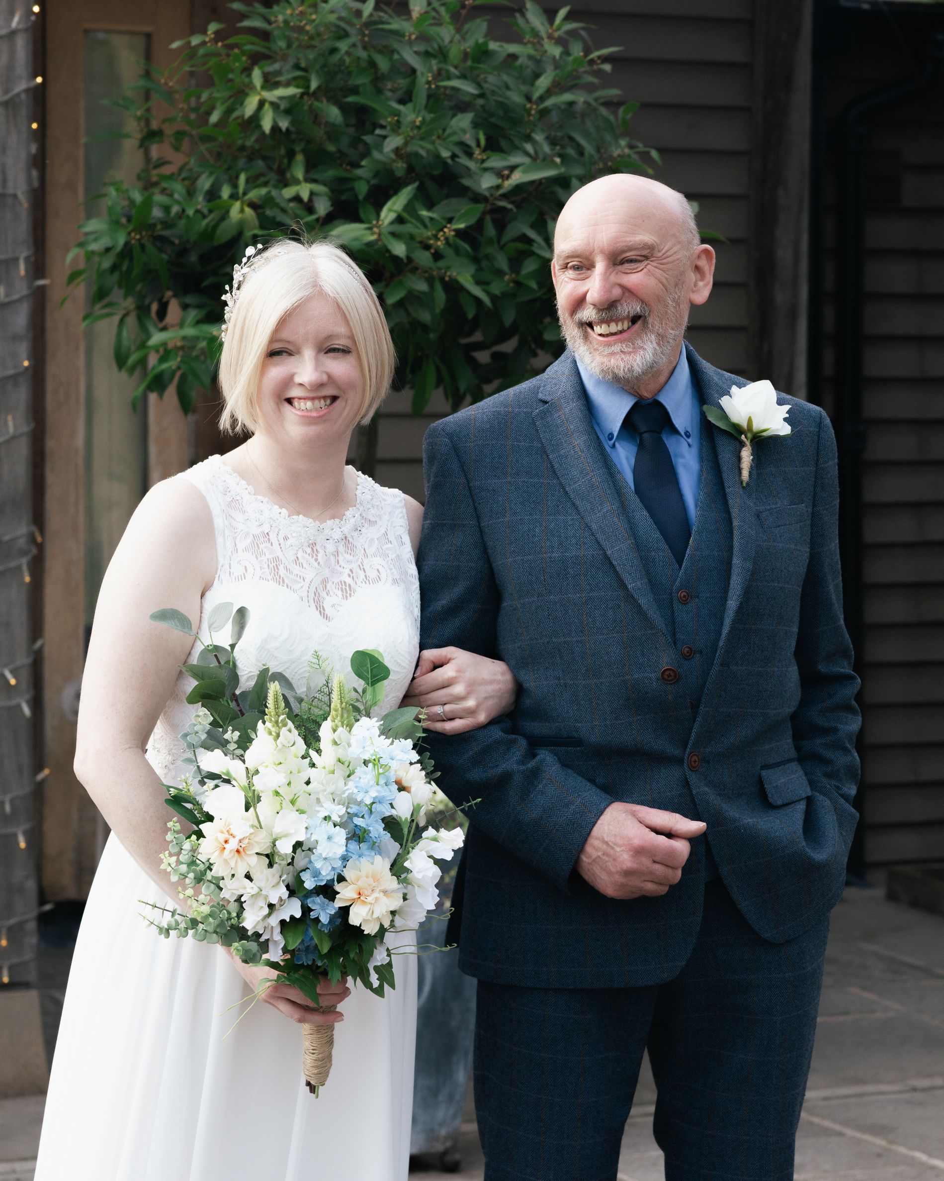 A bride in a white dress holds a pastel bouquet while posing with someone in a navy suit. Chester Wedding