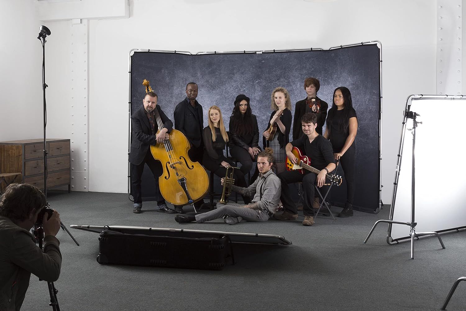 Music group posed together with instruments in a studio photoshoot setting against a dark backdrop.