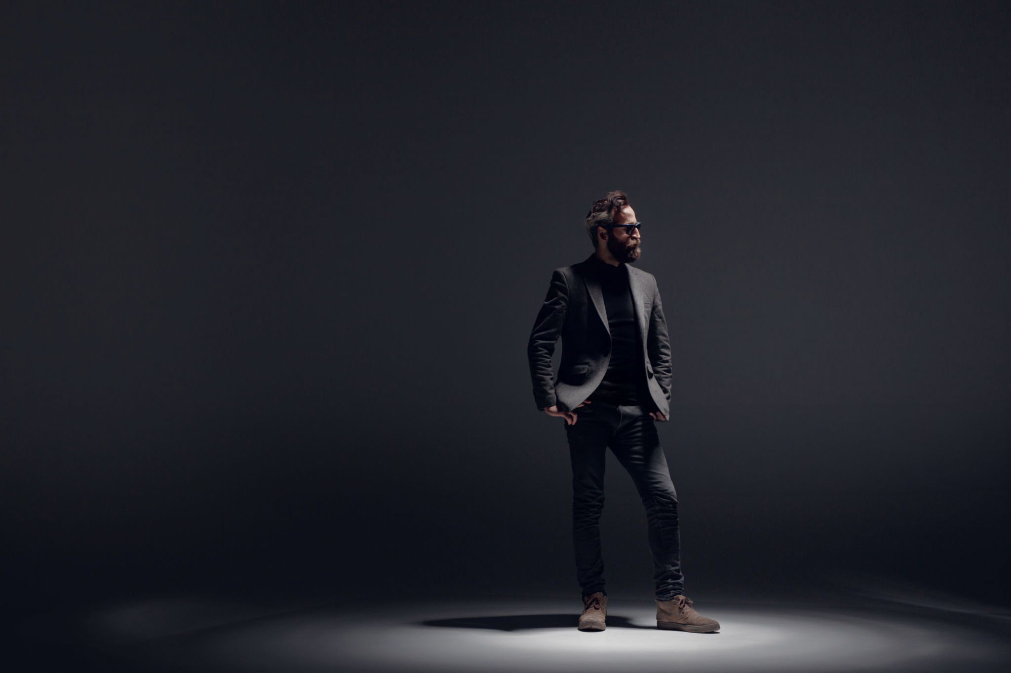 A performer's silhouette poses dramatically under spotlights in a dark professional studio setting.