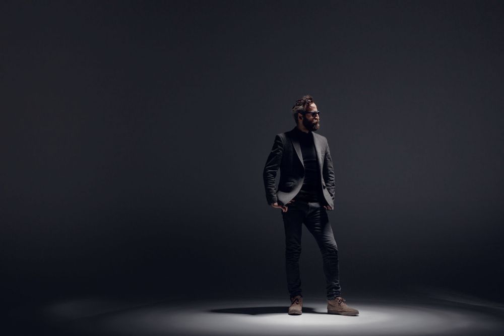 A performer's silhouette poses dramatically under spotlights in a dark professional studio setting.