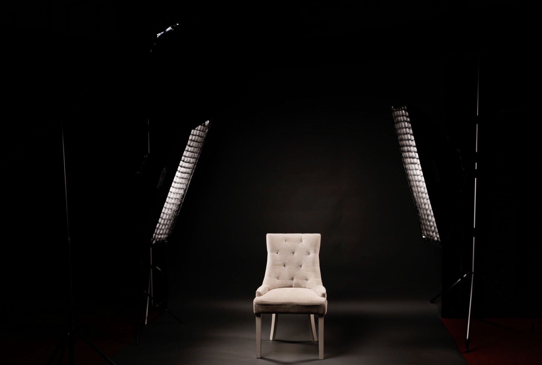 Empty upholstered chair positioned between two spiral lights in a dark dramatic studio setting.