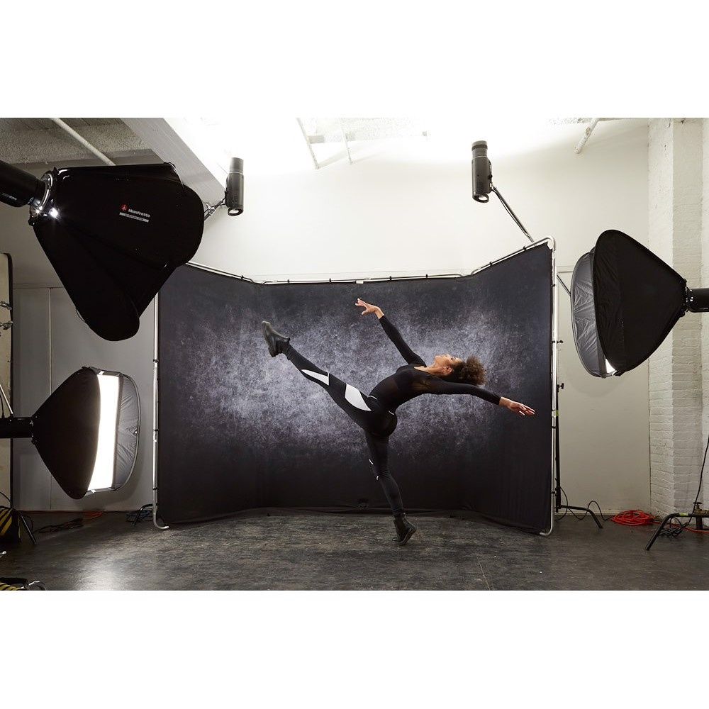 A dancer in a dramatic pose photographed in a studio with black backdrop and professional lighting equipment visible.