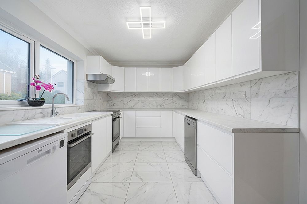 Luxurious modern kitchen with white marble countertops, sleek cabinets, and recessed lighting in an open-concept layout.