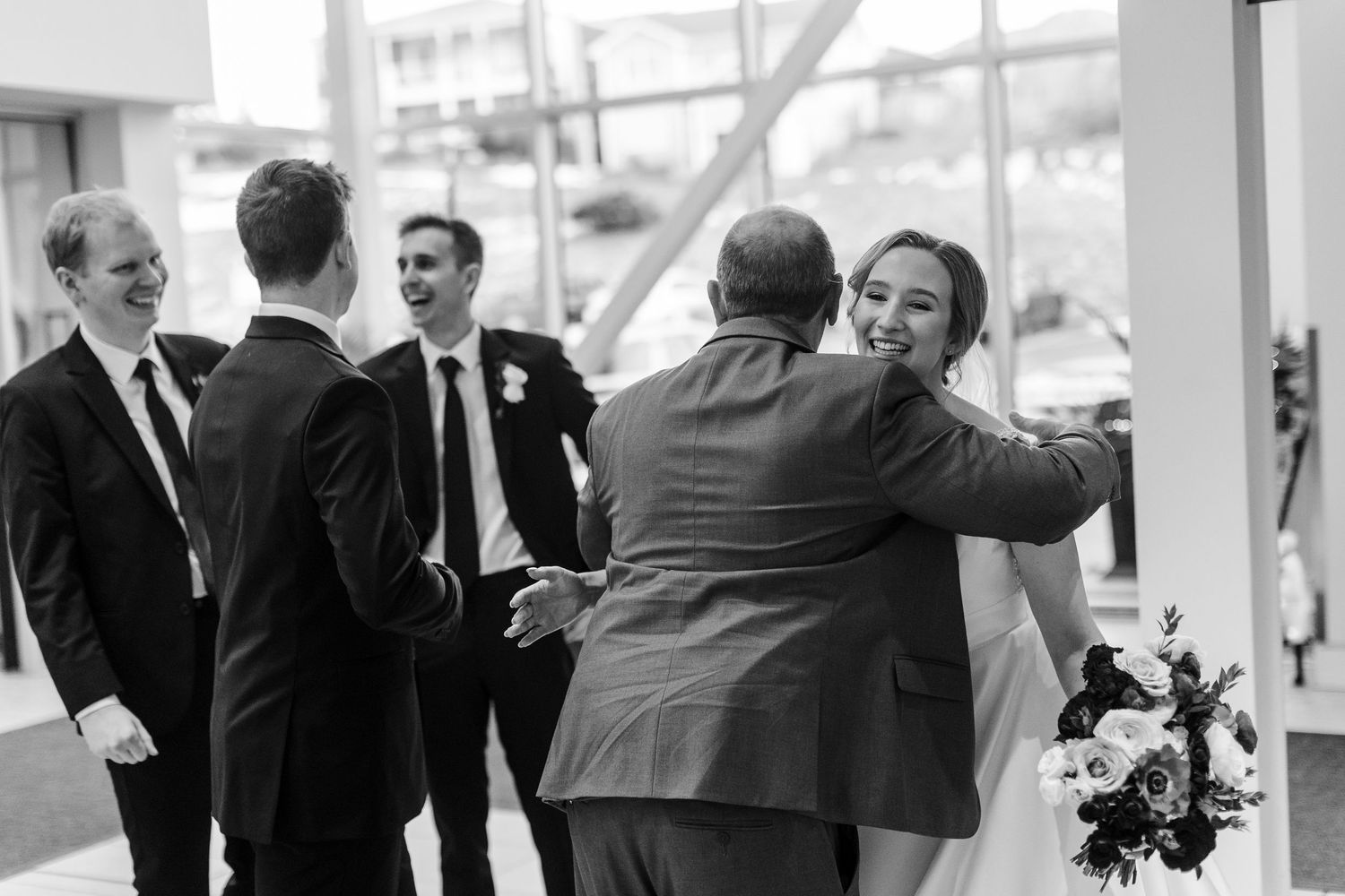 A candid black and white moment captured during a wedding reception as guests mingle and embrace.