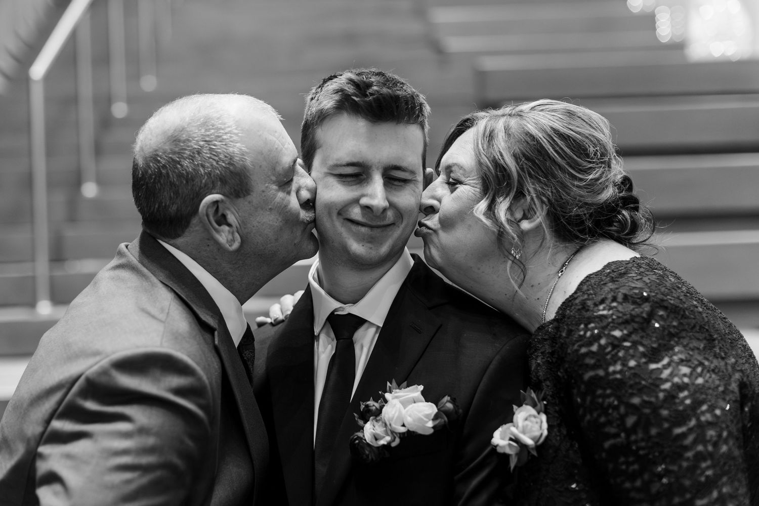 A candid black and white moment captured at a formal event showing three people sharing an intimate moment together.