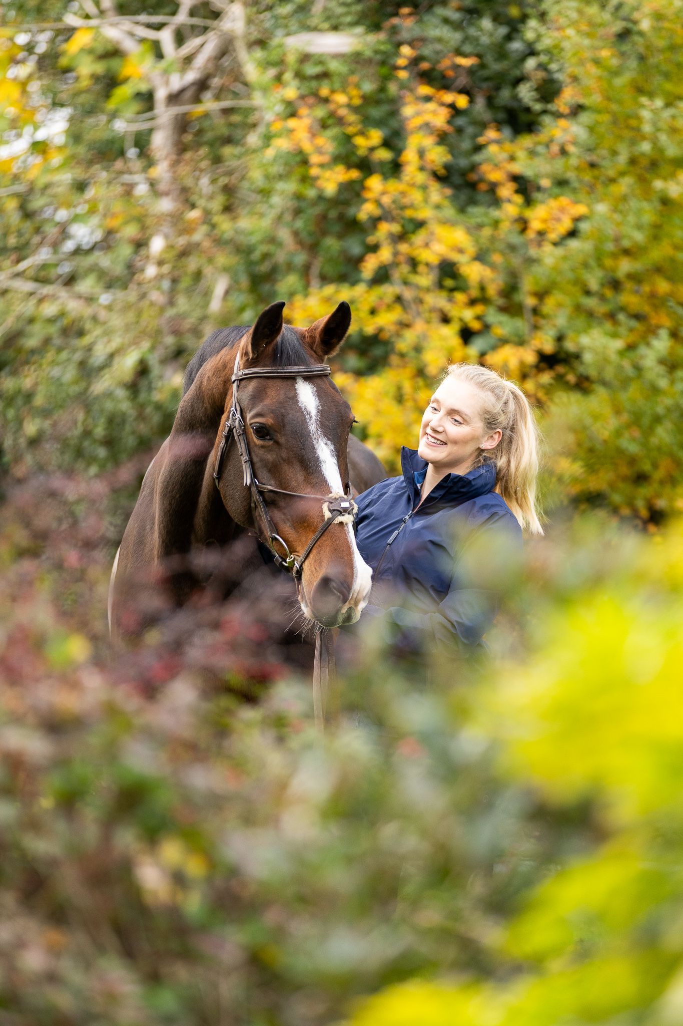 A group poses with horses along a tree-lined path during a sunny autumn day for outdoor photos.