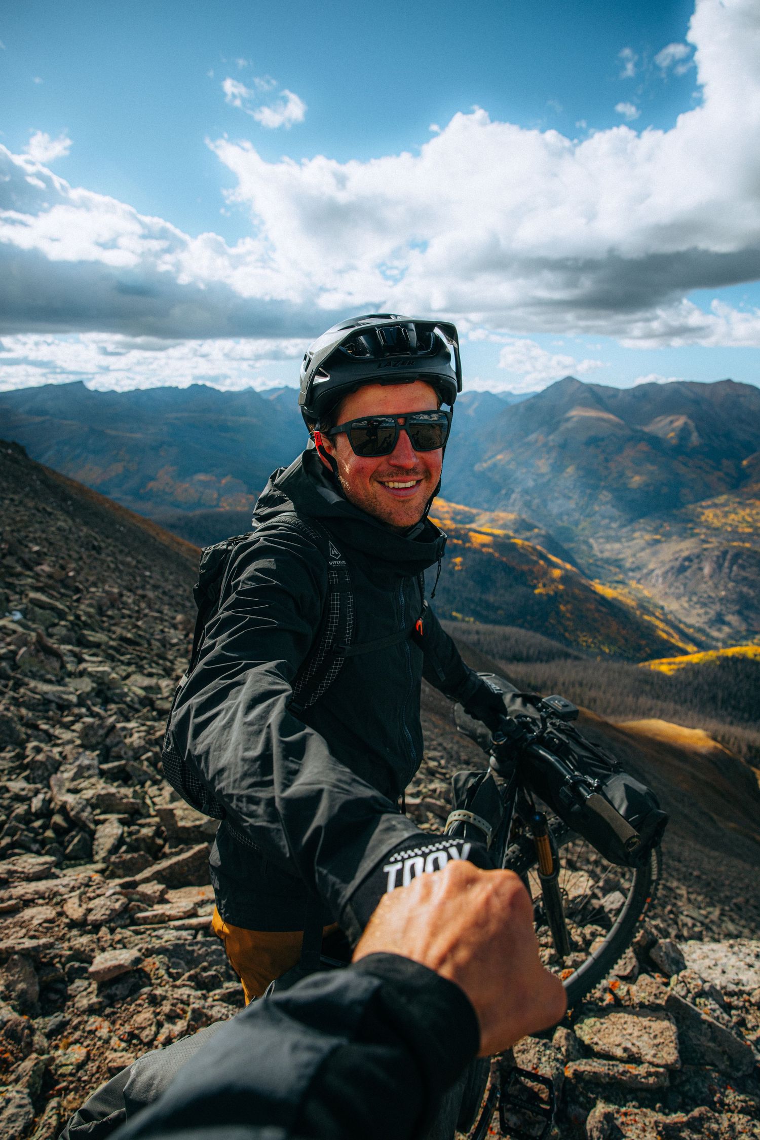 Mountain biking adventure in rugged alpine terrain with dramatic mountain peaks and cloudy skies in the background.