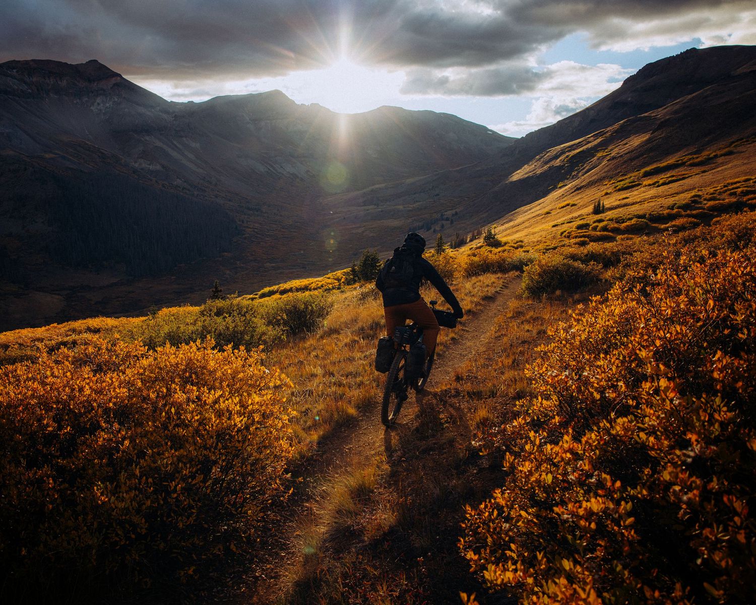 Scenic mountain landscape at sunset with golden light illuminating winding trails through rugged terrain.