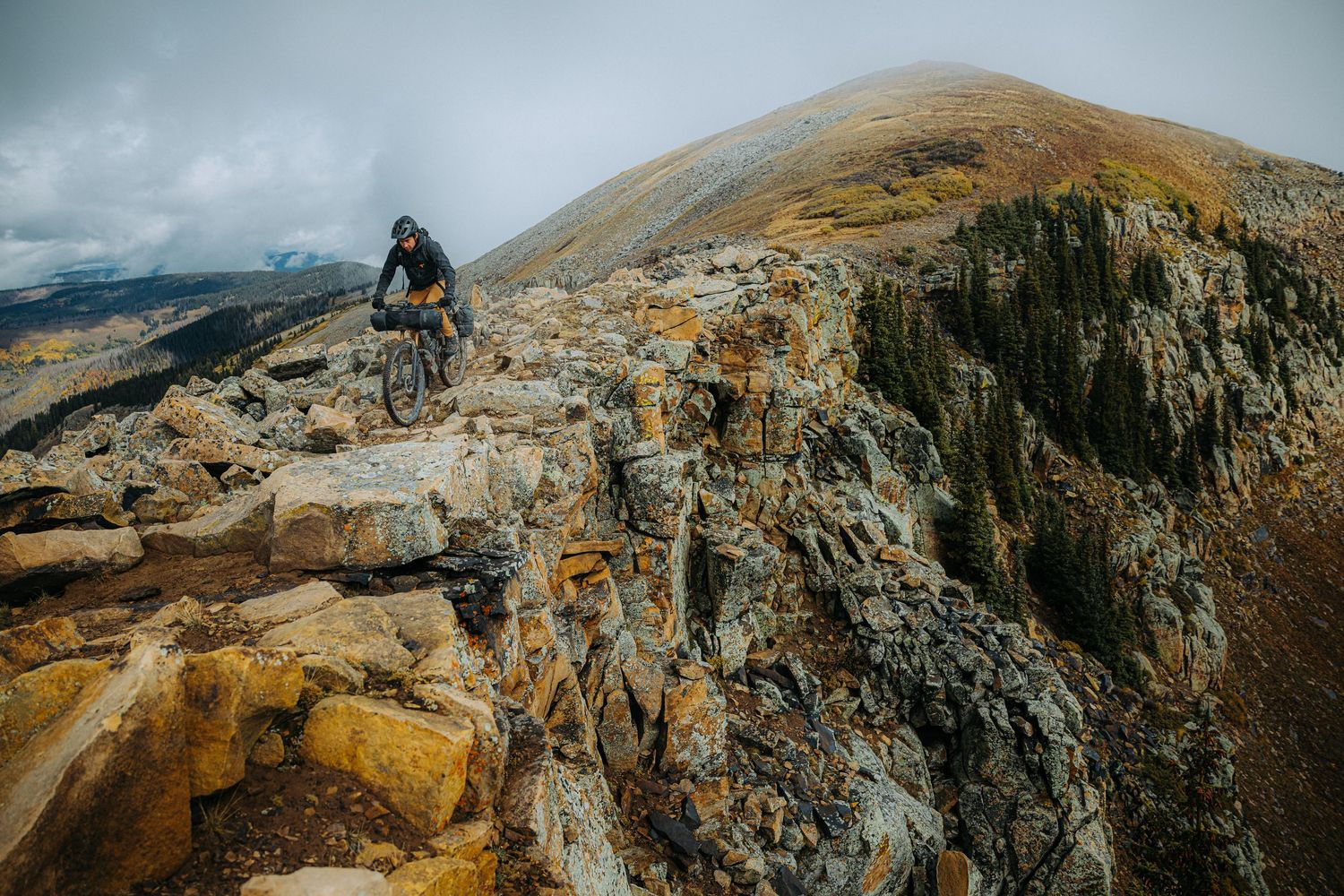 A mountain biker navigates rocky terrain along a dramatic ridgeline trail.