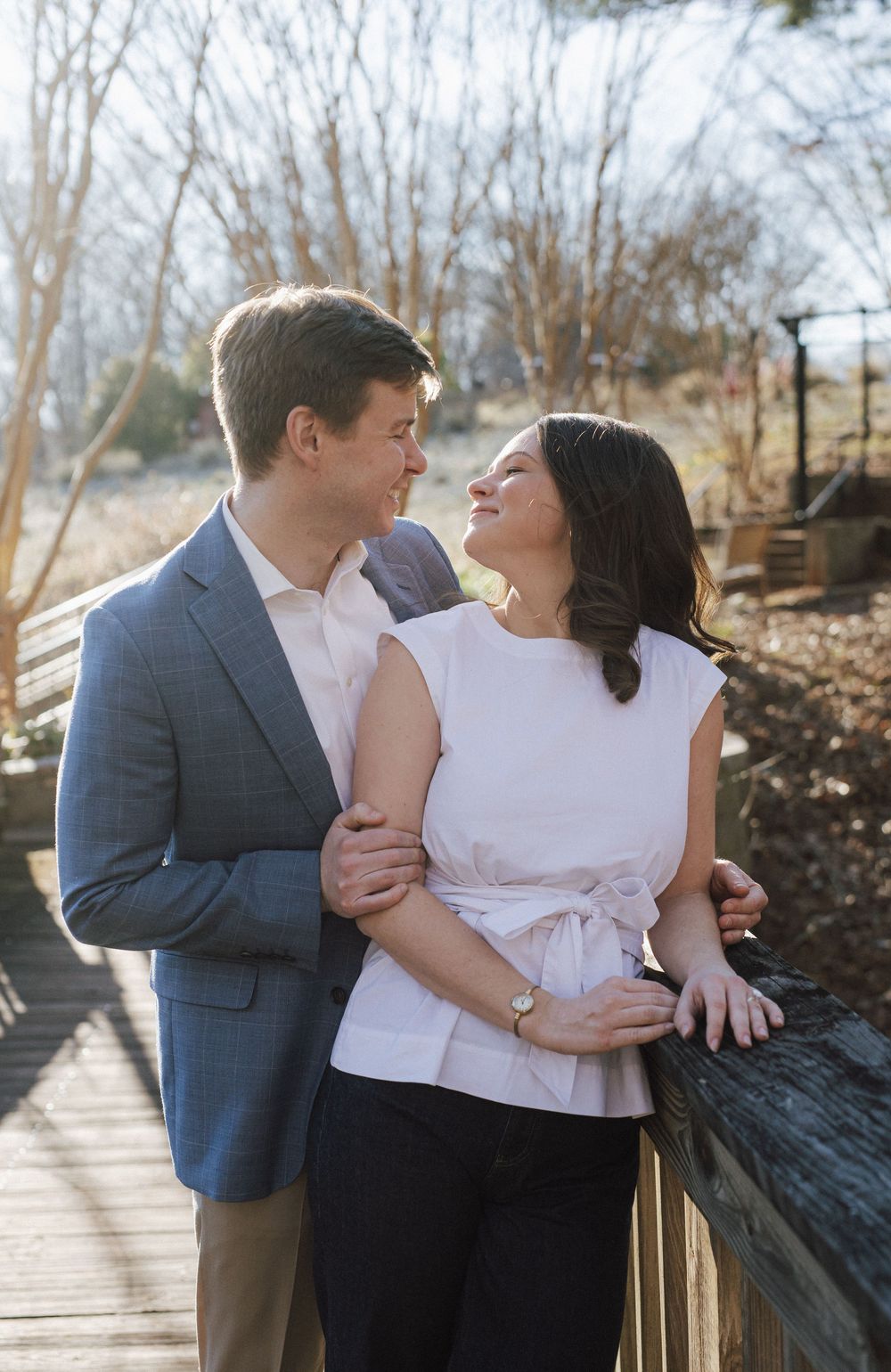 A couple sharing an affectionate moment while leaning against a wooden railing outdoors.