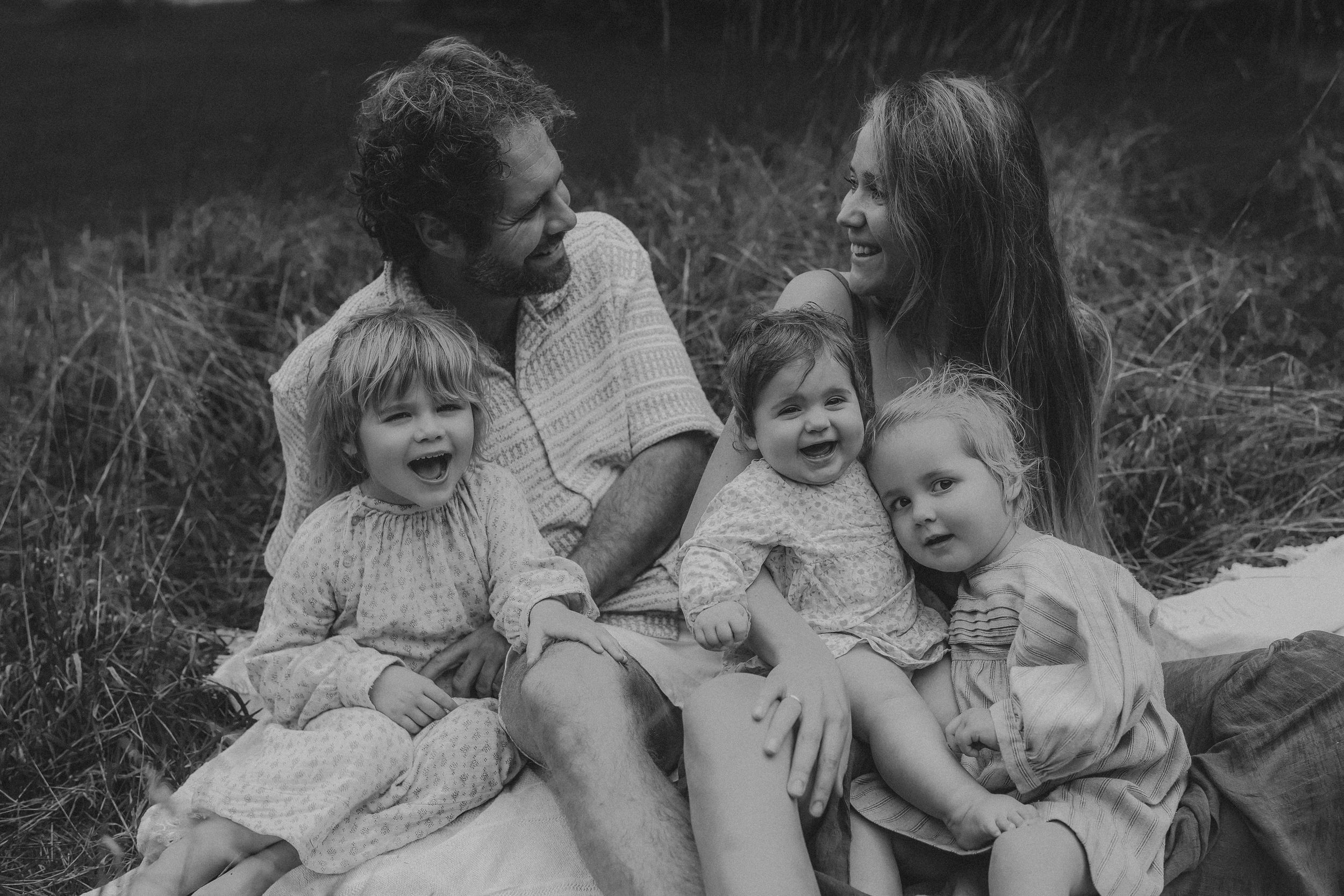 Black and white family portrait of parents smiling with three young children sitting on a blanket.