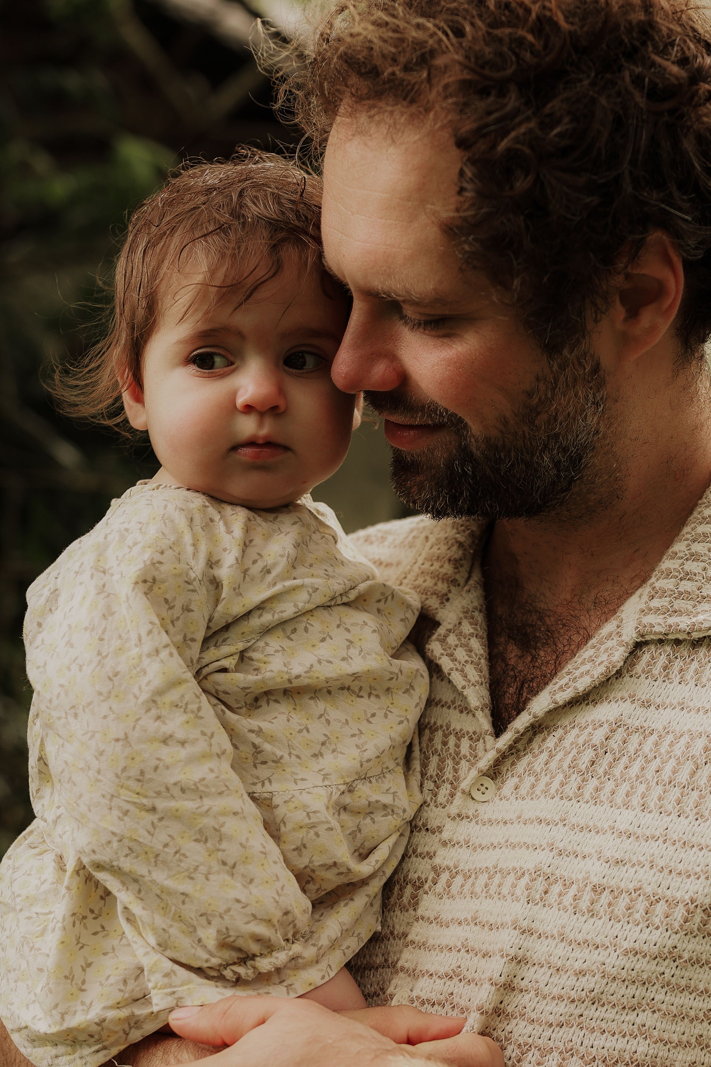 Tender moment of a bearded father holding his young baby close in a natural outdoor setting.