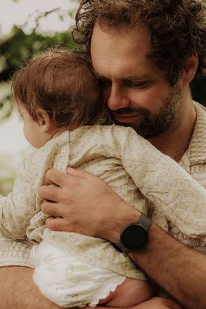 Loving father tenderly embracing his baby outdoors, wearing a watch in a natural setting.